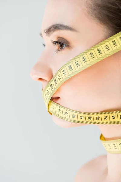 Side view of attractive young woman with closed mouth by measurement tape isolated on gray background — Stock Photo