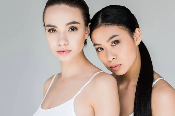 Portrait of attractive asian and caucasian young women looking at camera isolated on gray background — Stock Photo