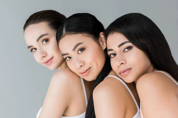 Portrait of attractive smiling multiethnic women looking at camera isolated on gray background — Stock Photo