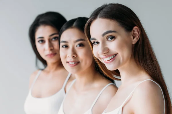 Attractive cheerful multicultural girls looking at camera, isolated on grey — Stock Photo