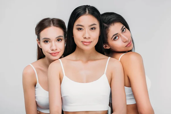 Attractive multicultural girls in white bras posing together, isolated on grey — Stock Photo