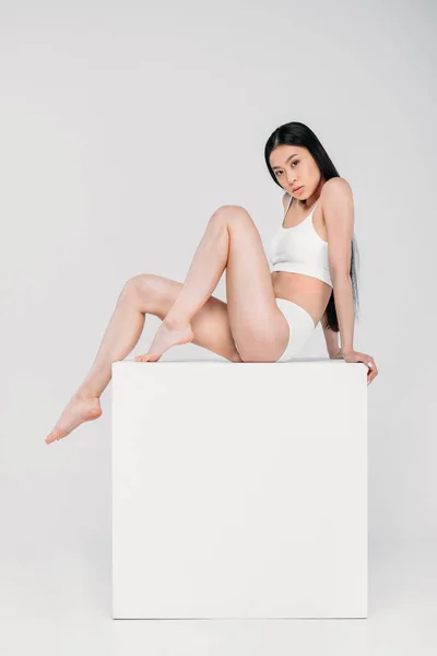 Attrayant asiatique fille en lingerie assis sur blanc cube, isolé sur gris — Photo de stock