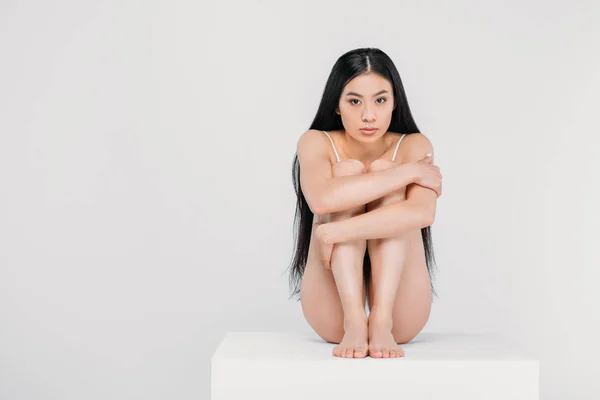 Beautiful young asian woman sitting on white cube, isolated on grey — Stock Photo