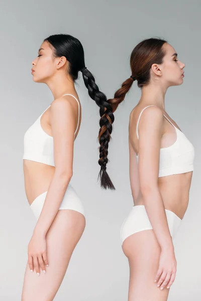 Elegantes chicas multiculturales atractivas con pelo en una trenza, aisladas en gris - foto de stock