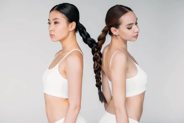 Привлекательные мультиэтнические девушки с волосами в одной косе, изолированные на серой — стоковое фото