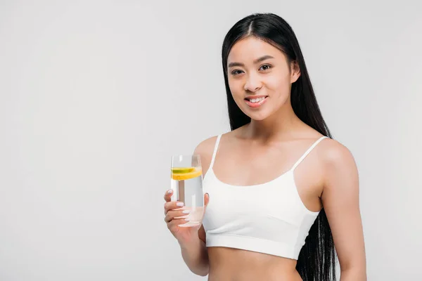 Élégante asiatique fille en soutien-gorge tenant verre d'eau, isolé sur gris — Photo de stock