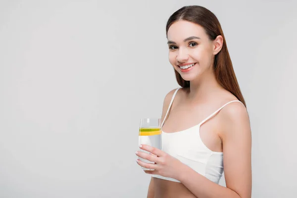 Красива усміхнена дівчина в бюстгальтері тримає лимонну воду в склі, ізольована на сірому — стокове фото