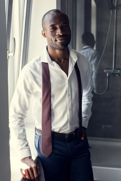 Handsome young businessman in white shirt with tie hanging on shoulders at bathroom — Stock Photo