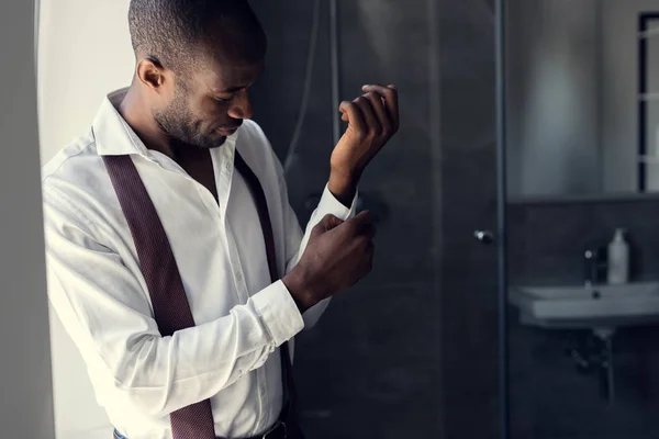 Handsome young businessman in white shirt buttoning cufflinks at bathroom — Stock Photo