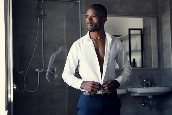 Продуманий бізнесмен, buttoning його білій сорочці у ванній кімнаті і дивитися вбік — стокове фото