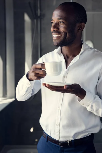 Happy young businessman in white shirt drinking coffee and looking away — Stock Photo