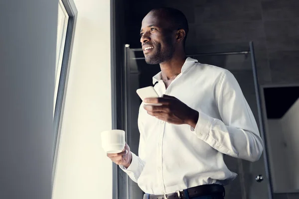 Vista dal basso di felice giovane uomo d'affari in camicia bianca utilizzando smartphone durante la pausa caffè — Foto stock