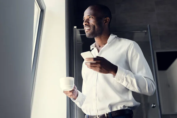 Bottom view of happy young businessman in white shirt using smartphone during coffee break — Stock Photo