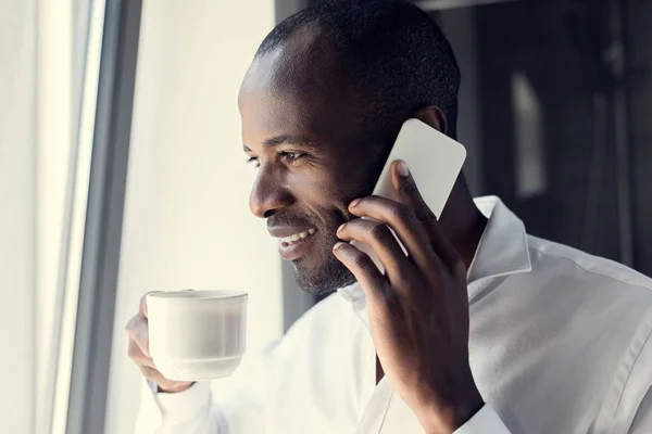 Smiling young businessman in white shirt talking by phone during coffee break — Stock Photo
