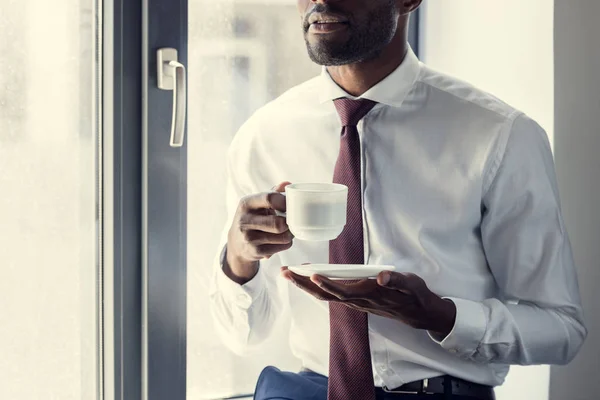 Colpo ritagliato di giovane uomo d'affari con una tazza di caffè davanti alla finestra — Foto stock