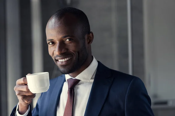 Sonriente joven hombre de negocios con taza de café mirando a la cámara - foto de stock