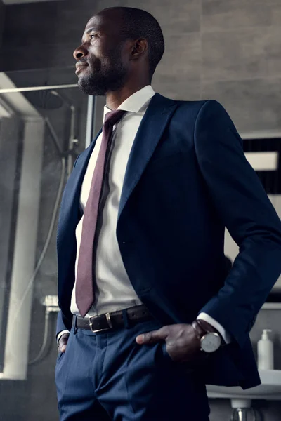 Young businessman in stylish suit standing in bathroom and looking away — Stock Photo