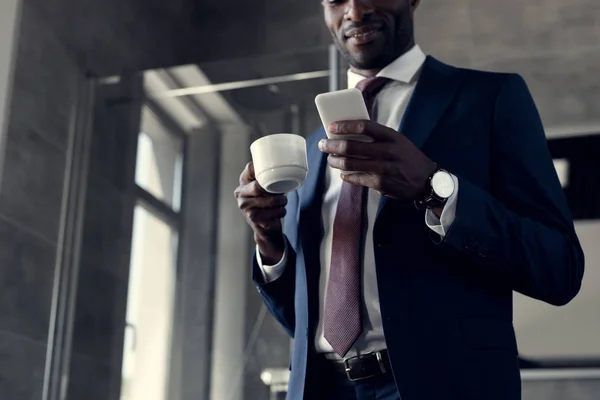 Vista dal basso di bel giovane uomo d'affari con tazza di caffè utilizzando smartphone in bagno — Foto stock
