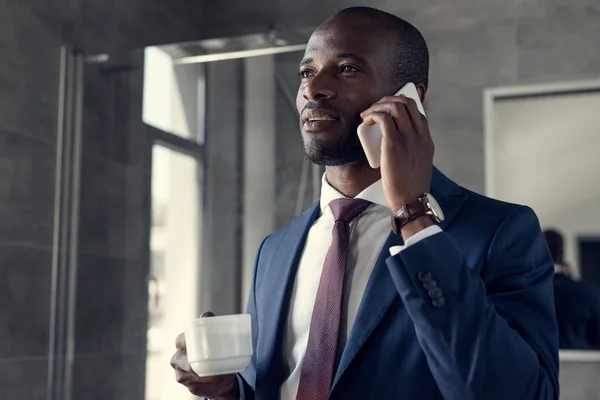 Jovem empresário elegante com xícara de café falando por telefone — Fotografia de Stock