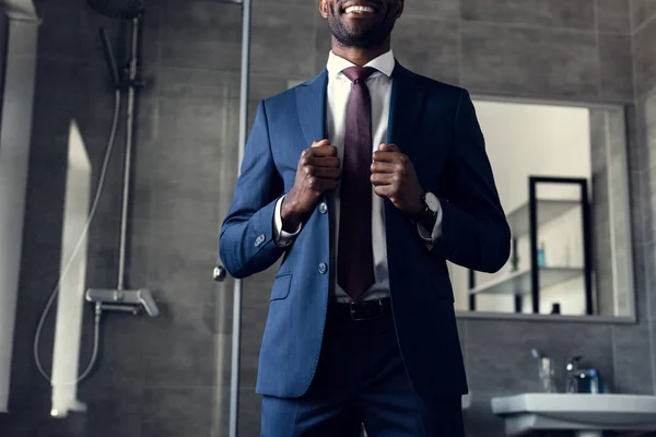 Tiro cortado de sorrir jovem empresário em terno elegante em pé no banheiro — Fotografia de Stock