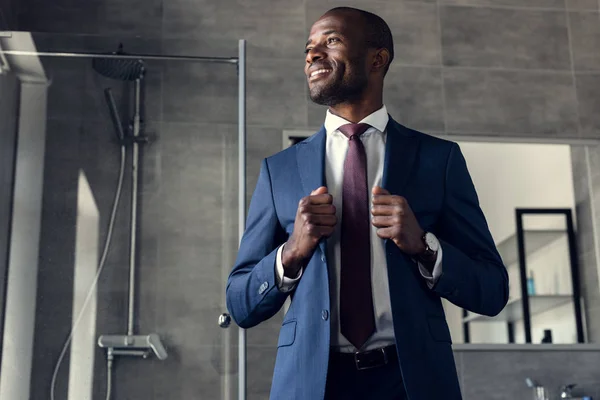 Bonito jovem empresário no elegante terno de pé no banheiro e olhando para longe — Fotografia de Stock