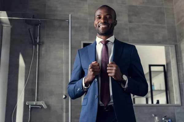 Jovem empresário bonito em terno elegante em pé no banheiro e olhando para a câmera — Fotografia de Stock