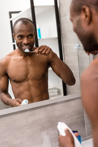Jovem feliz escovando os dentes enquanto olha para o espelho no banheiro de manhã — Fotografia de Stock