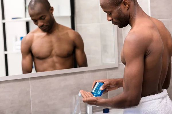 Guapo joven vertiendo después de afeitarse loción en la mano en el baño - foto de stock