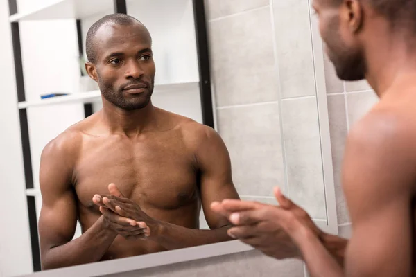 Schöner junger Mann, der im Badezimmer in den Spiegel schaut — Stockfoto