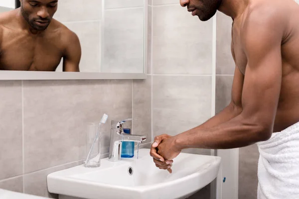 Cropped shot of young african american man in towel washing hands in bathroom — Stock Photo