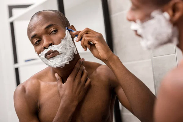 Foco seletivo do homem afro-americano bonito barbear com espuma e navalha — Fotografia de Stock