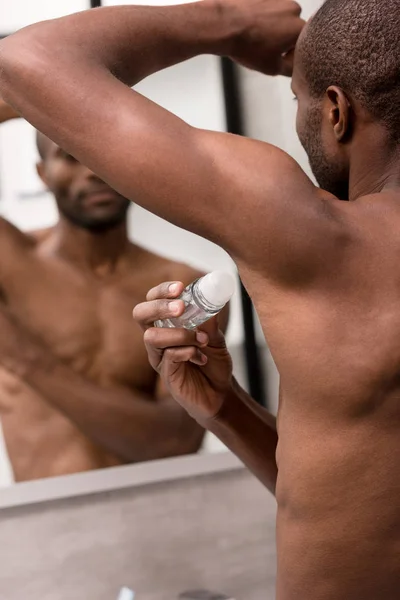 Tiro recortado de pecho desnudo hombre afroamericano sosteniendo antitranspirante en el baño - foto de stock