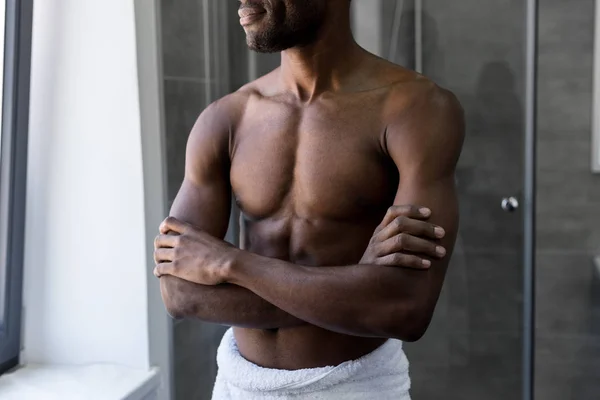Cropped shot of smiling african american man in towel standing with crossed arms in bathroom — Stock Photo