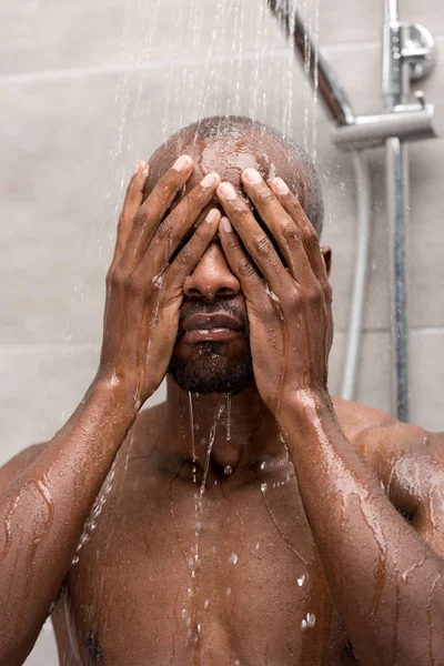 Joven africano americano hombre lavado cara y cuerpo en ducha - foto de stock