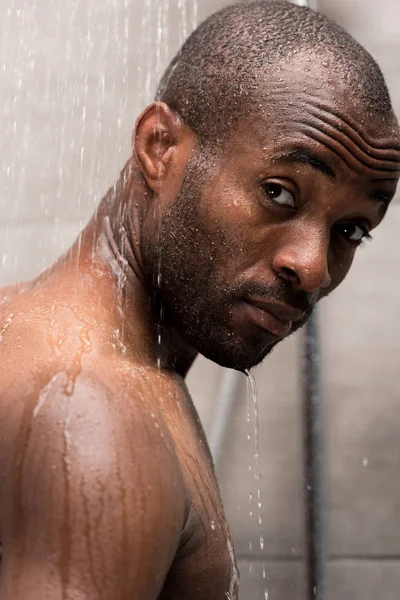 Vue rapprochée du jeune homme afro-américain se lavant sous la douche et regardant la caméra — Photo de stock