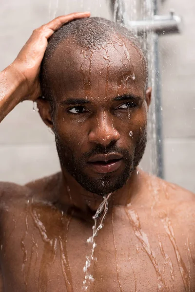 Vue rapprochée du jeune homme afro-américain se lavant sous la douche et regardant ailleurs — Photo de stock