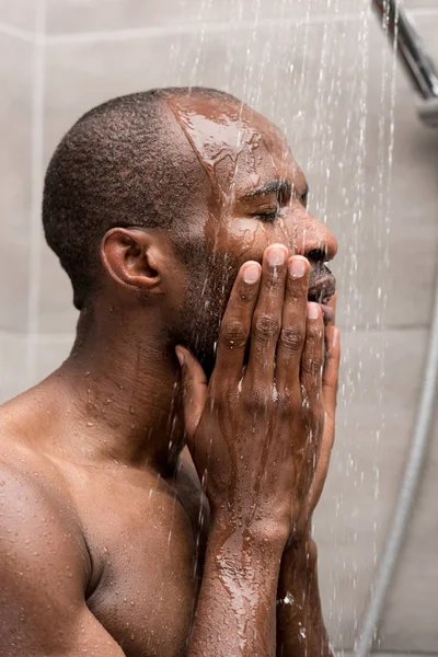 Nahaufnahme eines jungen afrikanisch-amerikanischen Mannes, der sich unter der Dusche sein Gesicht wäscht — Stockfoto