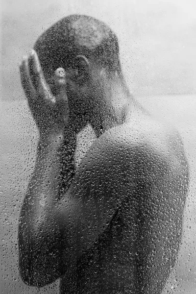 Side view of young african american man washing body in shower, black and white photo — Stock Photo
