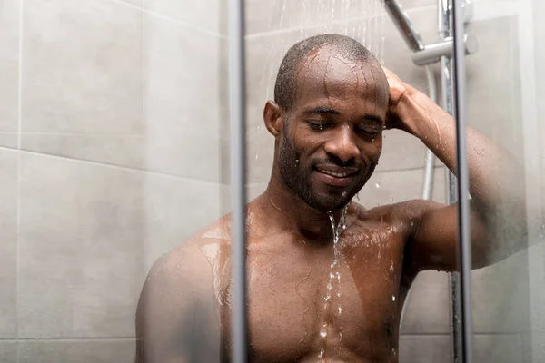 Bello sorridente africano americano uomo con gli occhi chiusi prendendo doccia — Foto stock