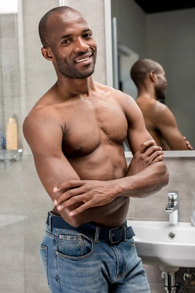 Schöner hemdloser afrikanisch-amerikanischer Mann, der mit verschränkten Armen im Badezimmer in die Kamera lächelt — Stockfoto