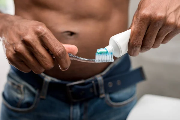 Primer plano vista parcial de joven afroamericano hombre sosteniendo cepillo de dientes y pasta de dientes — Stock Photo