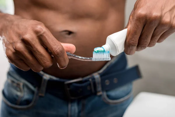 Primer plano vista parcial de joven afroamericano hombre sosteniendo cepillo de dientes y pasta de dientes - foto de stock