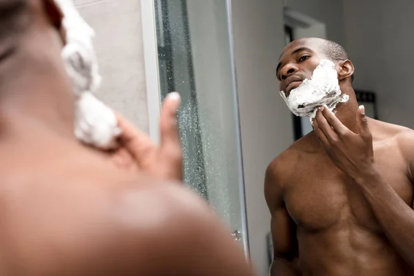 Cropped shot of handsome african american man shaving and looking at mirror — Stock Photo