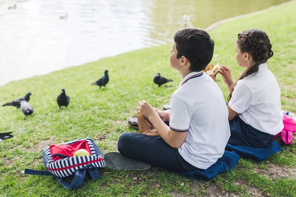 Adorables escolares sentados en la hierba y alimentando aves - foto de stock