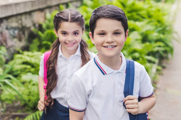 Adorable schoolchildren with backpacks looking at camera in park — Stock Photo