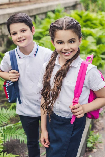 Schoolchildren with backpacks looking at camera in park — Stock Photo