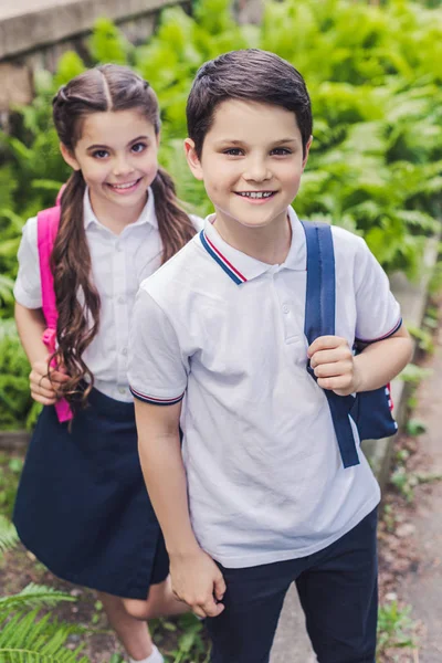 Crianças escolares felizes com mochilas olhando para a câmera no parque — Fotografia de Stock