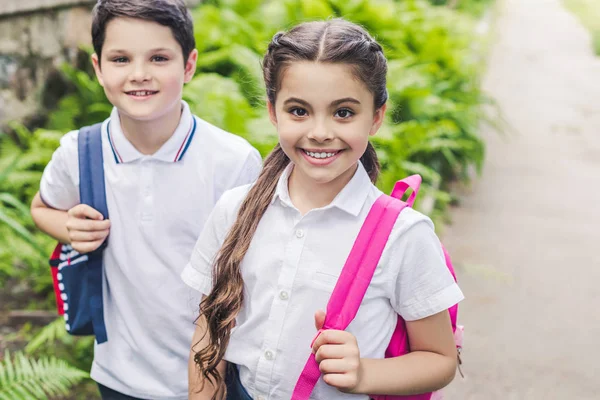 Lächelnde Schulkinder mit Rucksäcken blicken im Park in die Kamera — Stockfoto