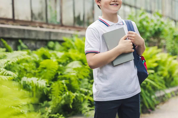 Cropped shot of schoolboy with backpack and book in garden — Stock Photo