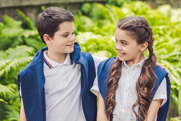 Kids in white shirts and jumpers over shoulders looking at each other in park — Stock Photo